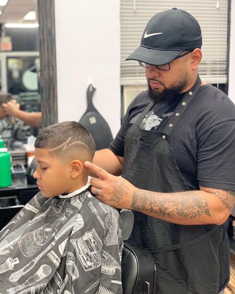 Barber finishing kid's skin fade with line design